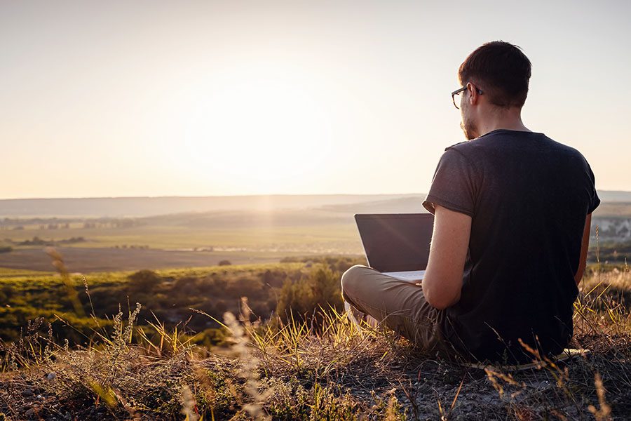 Client Center - Man Sitting on an Open Field in the Countryside Using His Laptop