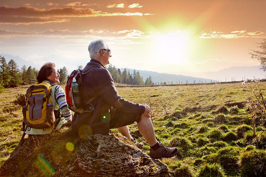 Employee Benefits - Older Couple Sitting on a Rock Watching the Sunset After Hiking